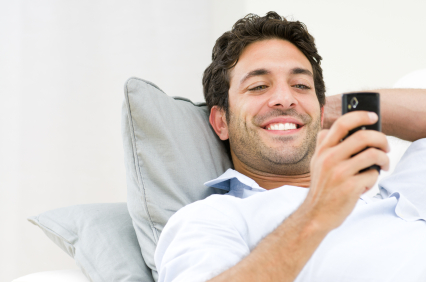 Beautiful young man relaxing on sofa and looking at his smart phone